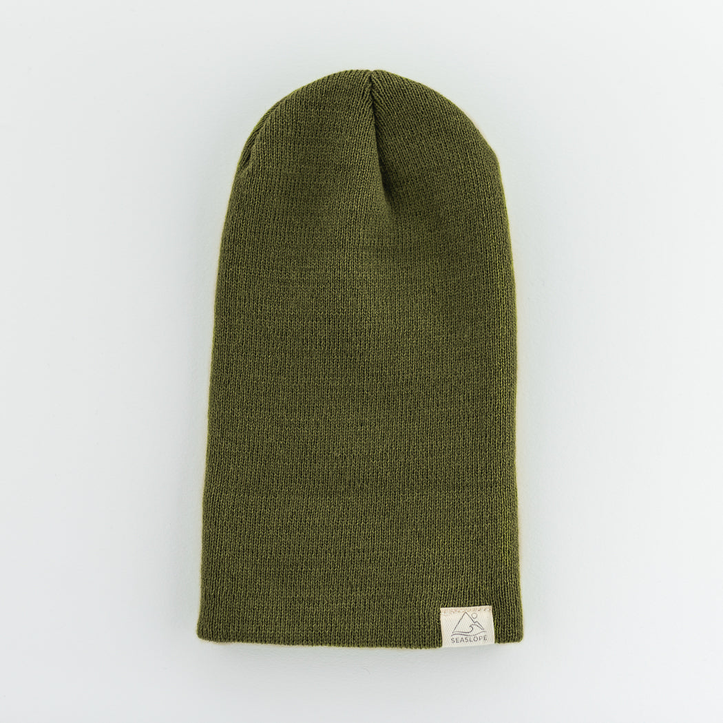 The infant/toddler beanie is a green knit hat designed for comfort and flexibility. It features a soft, stretch fit and has a small beige label on the brim, displayed against a light background.