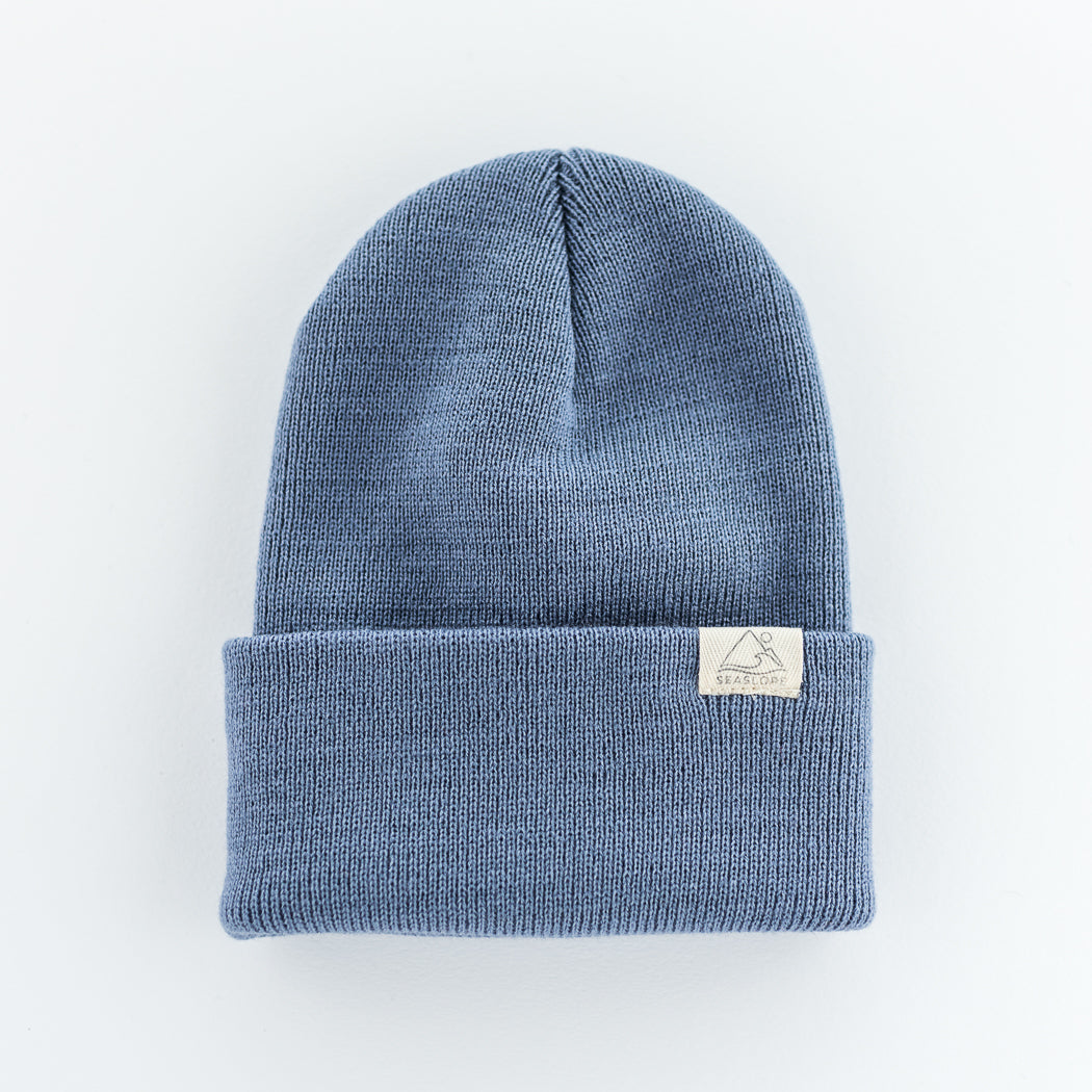 The description portrays a blue infant/toddler beanie from the Seaslope1 brand, made entirely of acrylic. This beanie showcases a folded cuff design and is set against a light background to highlight its features. A notable detail is the small white rectangular patch on the beanie, which includes a design and text that emphasizes its American craftsmanship.