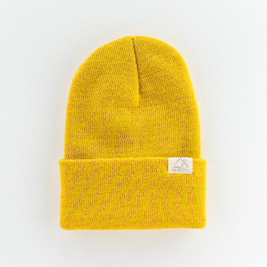 The SUN INFANT/TODDLER BEANIE by seaslope1 is a vibrant yellow beanie crafted from 100% acrylic, providing a soft and flexible fit. It features a folded cuff and includes a small white label with a minimalist mountain graphic on a light gray background.