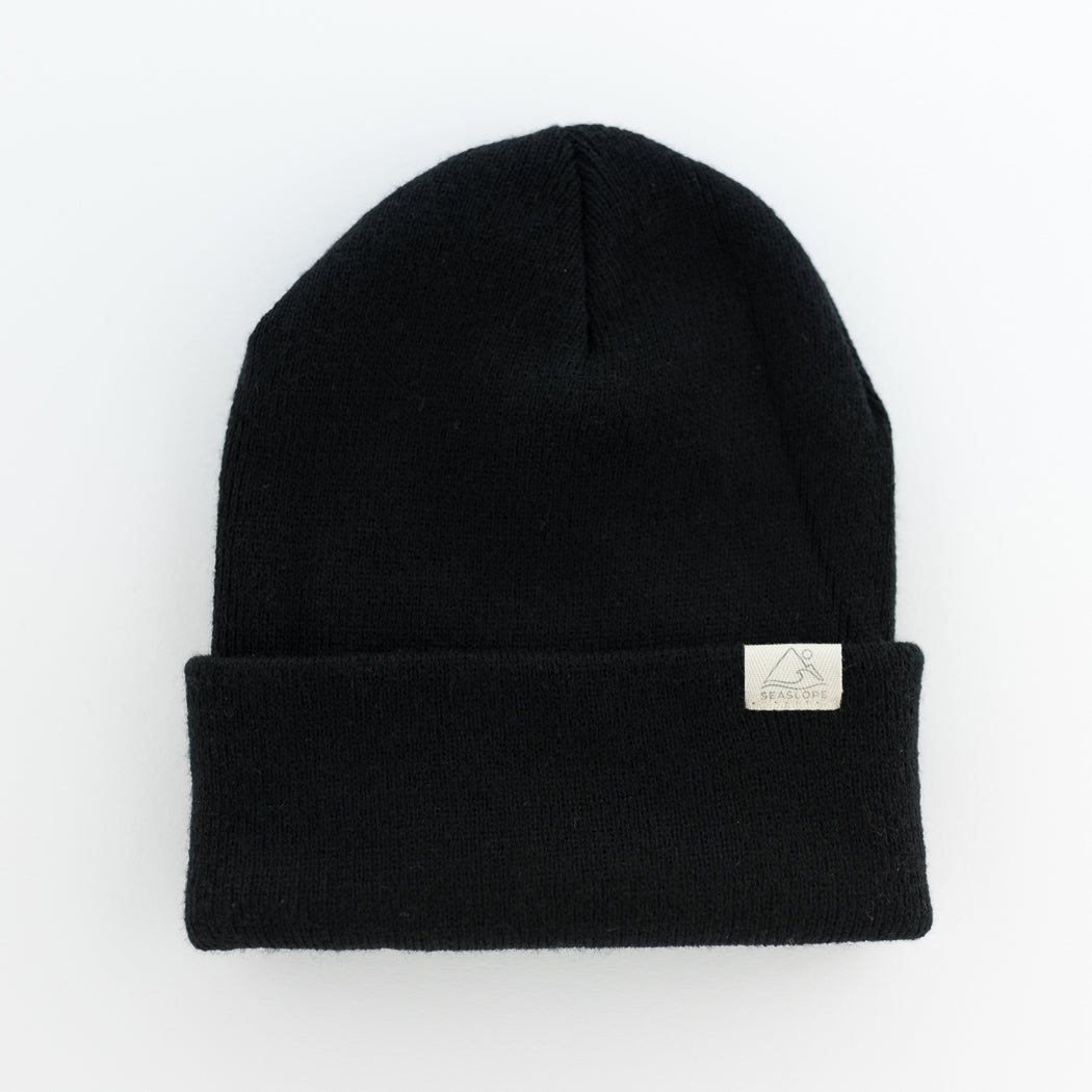 The JET Youth/Adult Beanie by seaslope1 is skillfully made from 100% acrylic yarn. Its sleek black knit design features a folded brim, adorned with a small rectangular label, adding to its understated elegance. Presented against a plain white background, this beanie embodies minimalist style.