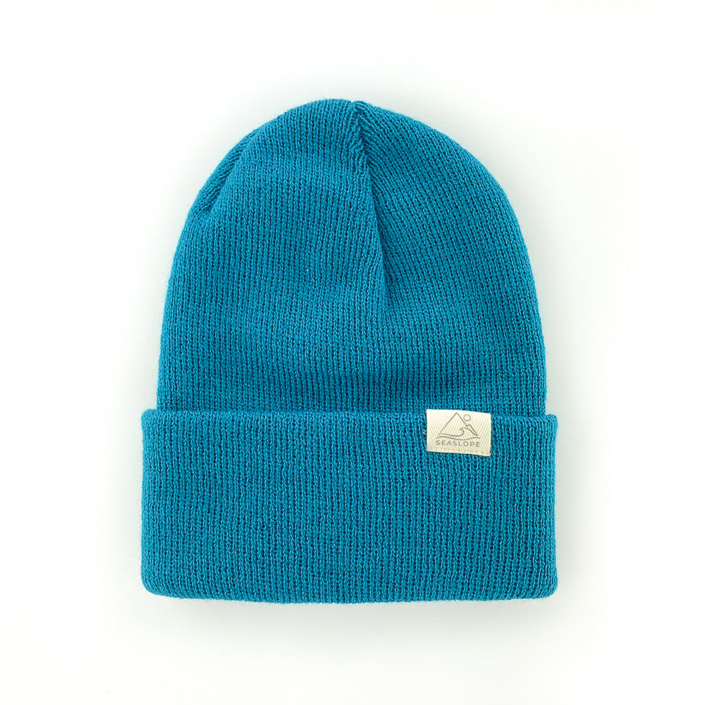 The GLACIER INFANT/TODDLER BEANIE from seaslope1 is crafted from 100% acrylic, offering a soft stretch fit for maximum comfort. It features a blue knit design with a folded brim and includes a small rectangular tag on the brim.