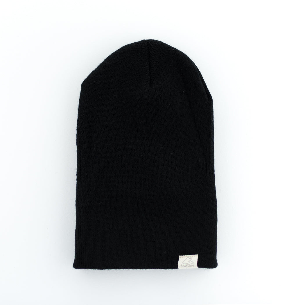 The JET YOUTH/ADULT BEANIE by seaslope1 is a stylish black knit accessory. Made in the USA from 100% acrylic, it offers warmth and comfort. The beanie features a small rectangular label near the edge with a minimalist design, adding to its sleek appearance.