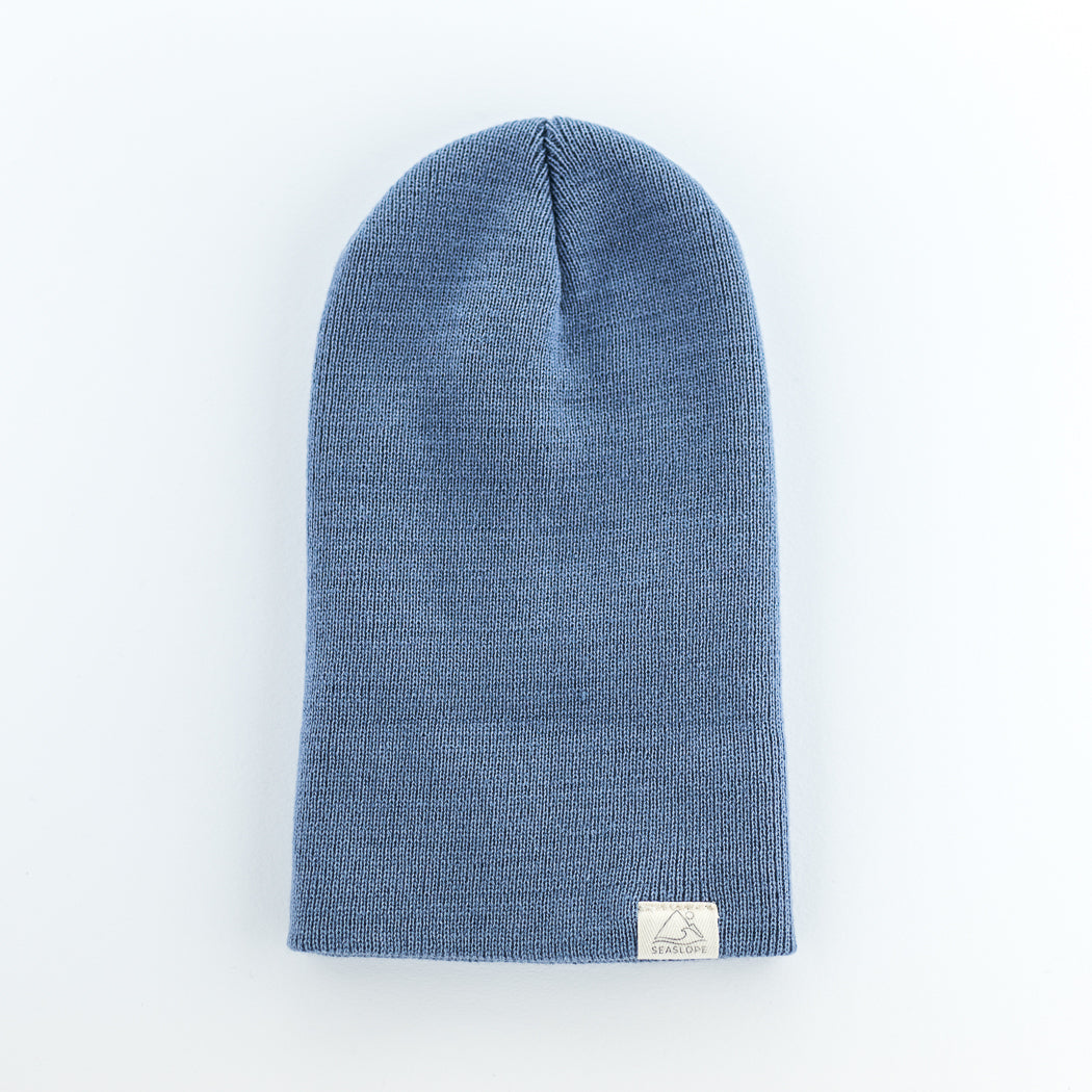 The PACIFIC INFANT/TODDLER BEANIE by seaslope1 is a stylish blue beanie made from 100% acrylic. Proudly crafted in the USA, this beanie features a small white tag stitched onto the bottom hem. Presented on a light grey background, it combines quality and fashion seamlessly.