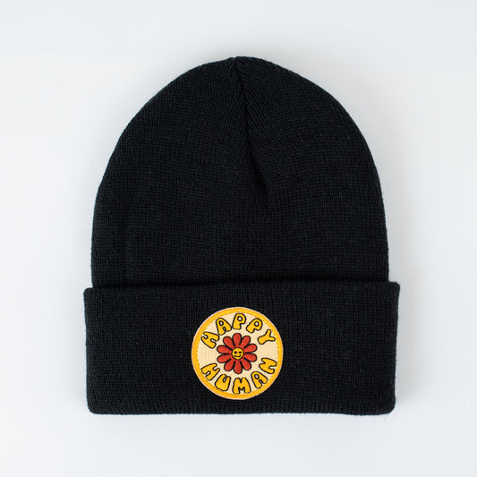 Introducing the Happy Human - Jet Black Kids Beanie. This American-made black knit beanie features a folded brim and a yellow circular patch. At the center is a delightful smiling flower, encircled by the embroidered words "HAPPY HUMAN.