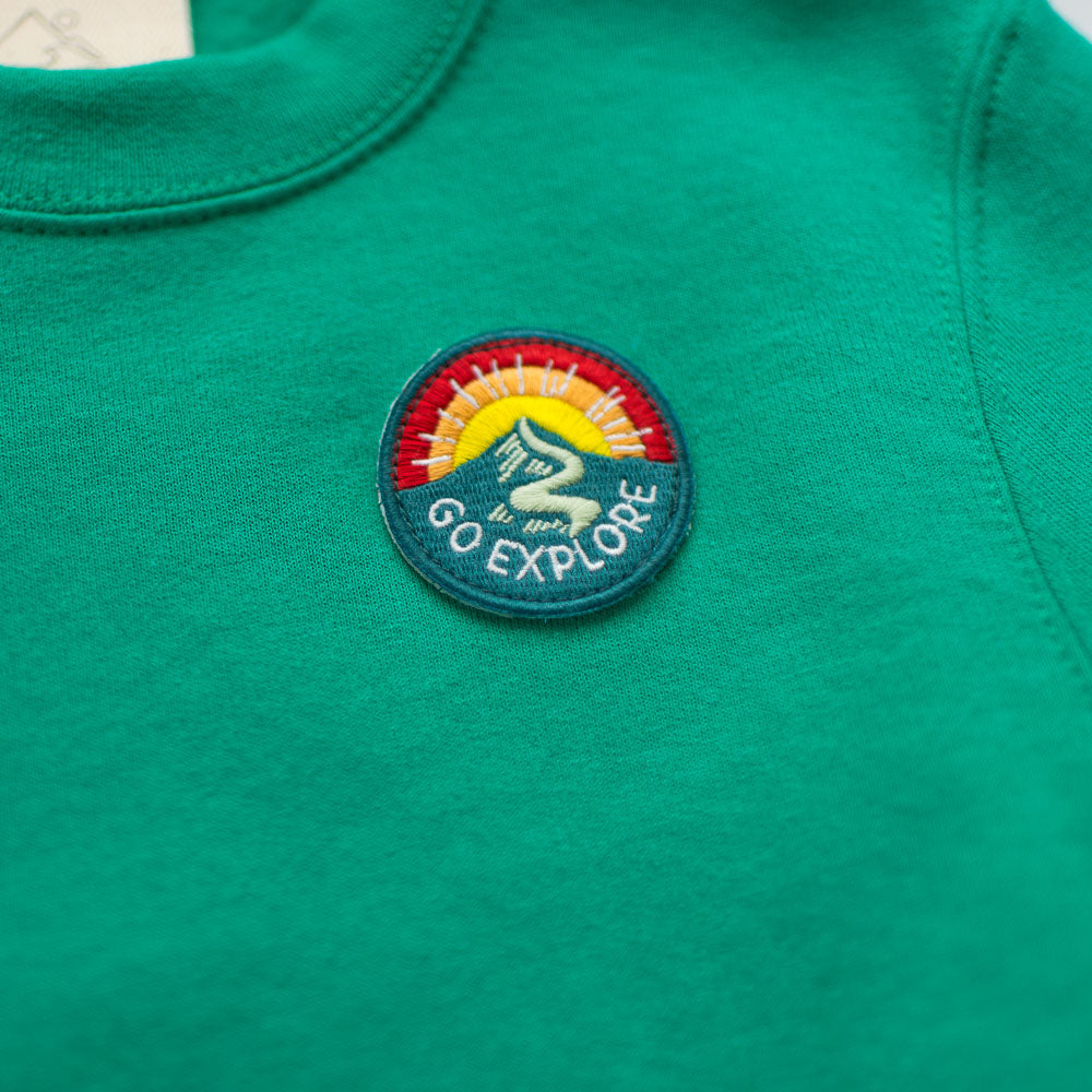 The Seaslope1 Go Explore Sweatshirt is a cozy green cotton pullover featuring an embroidered patch with a mountain, rising sun, river, and the phrase "Go Explore.