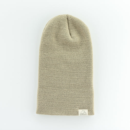 The SAND INFANT/TODDLER BEANIE by seaslope1 is a cozy, beige knitted hat designed for infants and toddlers. It offers a soft stretch fit and includes a small white label at the bottom edge. The beanie is proudly made in the USA and is depicted on a plain white background.