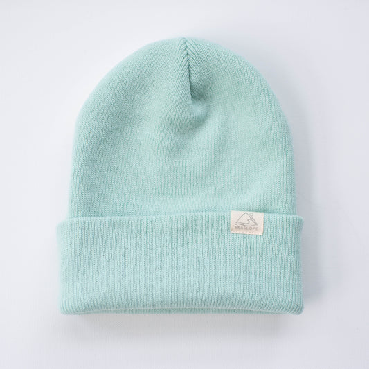 A seafoam youth/adult beanie from seaslope1, made entirely of acrylic in a light blue shade, features a folded brim. It is displayed on a white background with the brim showcasing a small white tag.