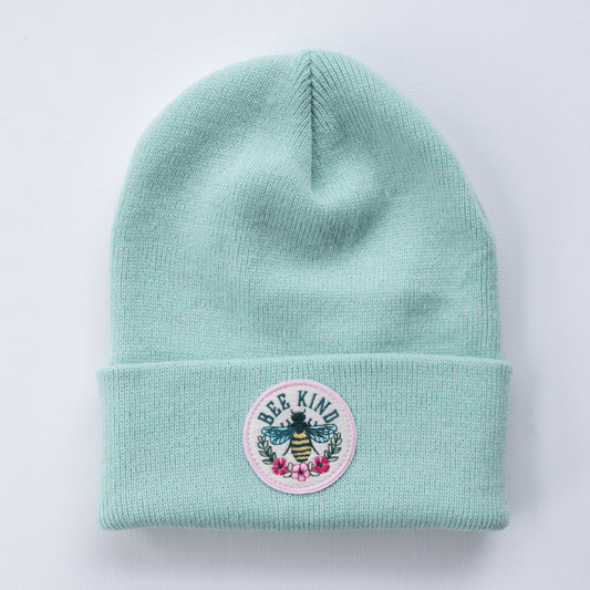 Introducing the Bee Kind | Seafoam - Adult Beanie, a stylish knit accessory in a trendy seafoam green. This beanie features a circular embroidered patch with an intricate design of a bee, surrounded by flowers and leaves, along with the words "Bee Kind.