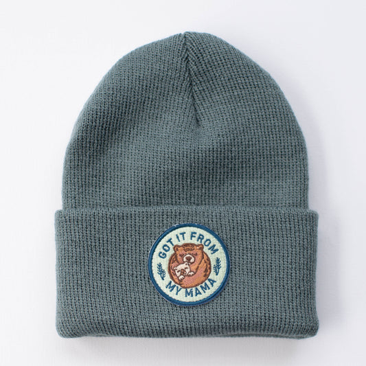 The Got it from my Mama - Spruce Kids Beanie by seaslope1 is crafted in the USA and features a gray 100% acrylic design. It is adorned with a circular patch that includes a bear illustration and the phrase "Got it from my mama" on a white background.