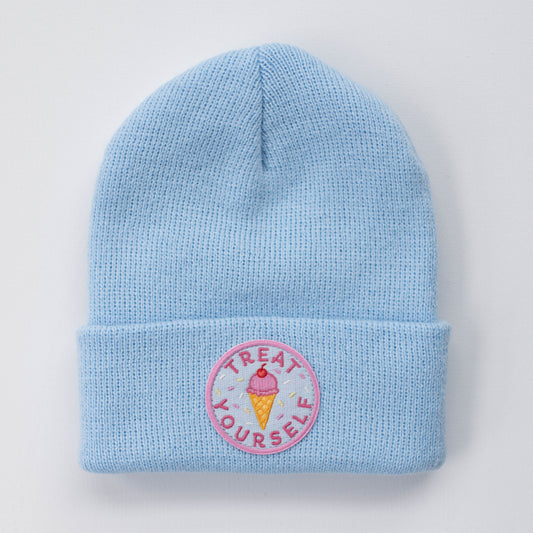 The TREAT YOURSELF SKY INFANT/TODDLER BEANIE by seaslope1 is crafted from 100% acrylic. It comes in a light blue shade and has a folded brim. The beanie is adorned with an embroidered circular patch that features an ice cream cone and the words "Treat Yourself" in pink.