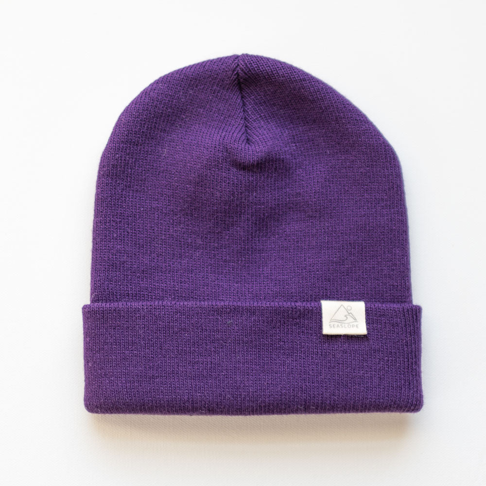 The PLUM YOUTH/ADULT BEANIE by seaslope1 is crafted in the USA and features a folded brim. It is adorned with a small white label. The beanie is set against a plain white background, highlighting its vibrant plum color and texture.