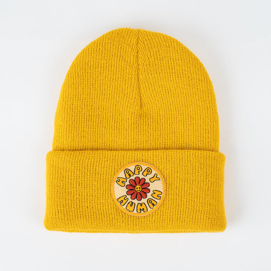 Introducing the seaslope1 Happy Human - Sun Kids Beanie: a vibrant yellow knit beanie designed for children. It features a folded brim adorned with a circular embroidered patch that showcases a cheerful red flower surrounded by the phrase "HAPPY HUMAN" on a solid white background.