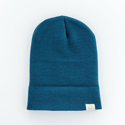 The TIDE YOUTH/ADULT BEANIE from seaslope1 is showcased against a white background. This blue beanie features a folded brim and is made from 100% acrylic, offering a soft stretch fit and showcasing a subtle ribbed pattern.