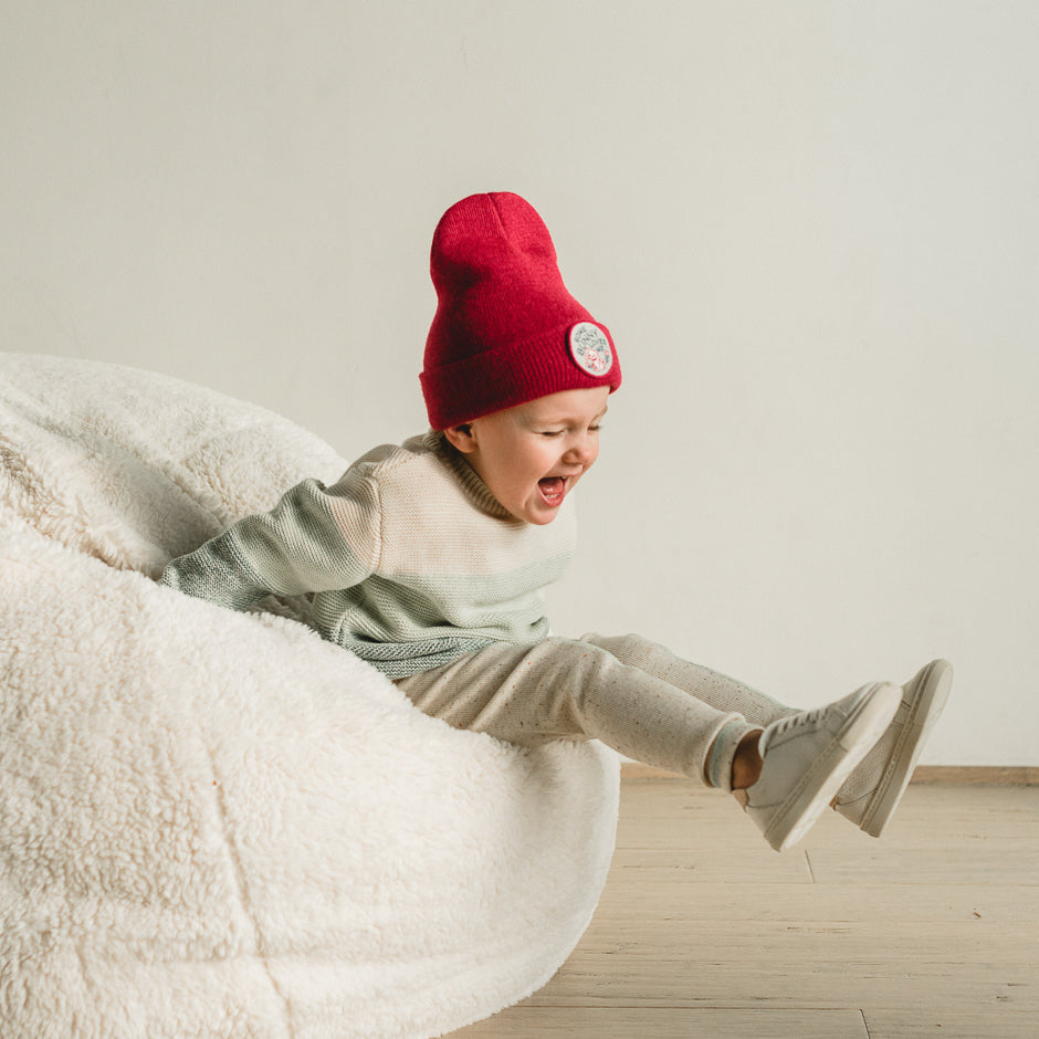 A child, dressed in light-colored clothes and wearing a charming beanie, joyfully slides off a plush white bean bag. The room's wooden floor and minimalist decor contribute to the cozy atmosphere.